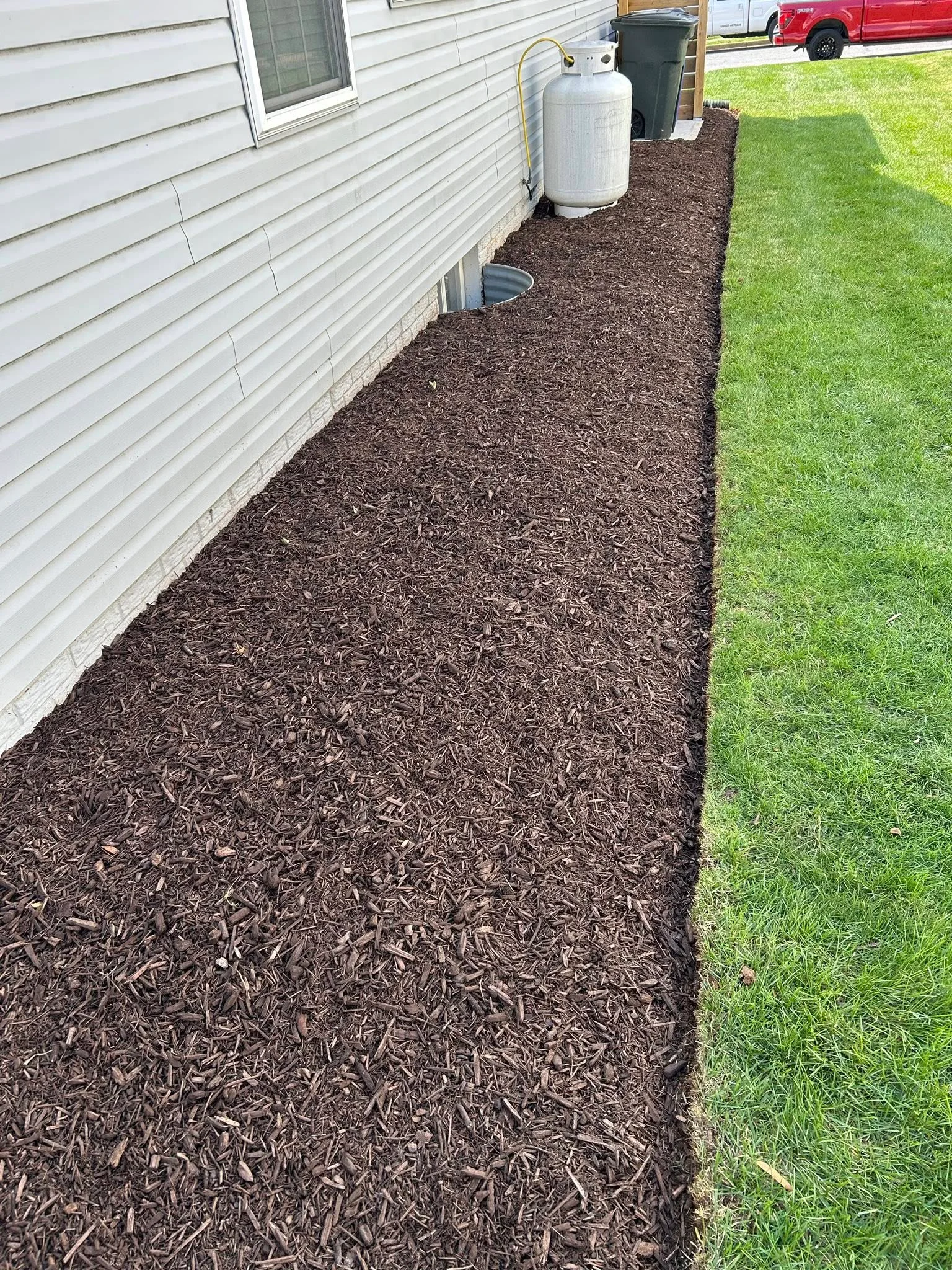 Dark mulch bed installed along white mobile home siding with clean lawn edge