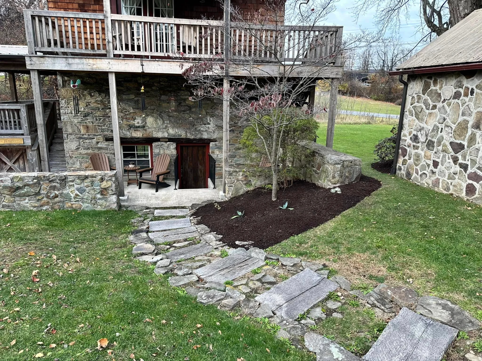 Flagstone pathway and dark mulch landscape bed installation at stone home foundation