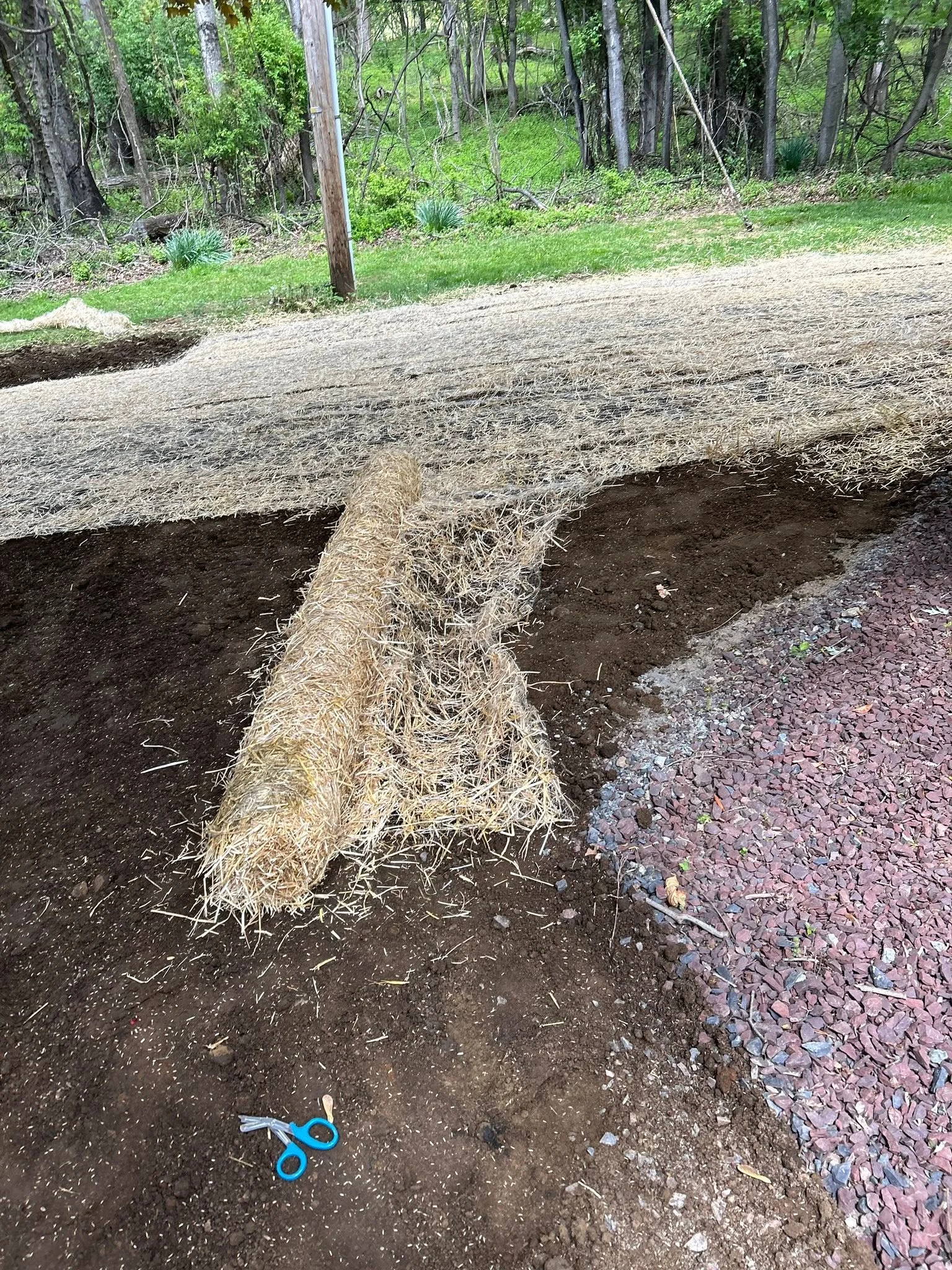 Erosion control matting and straw installed on sloped soil bed with red mulch edging