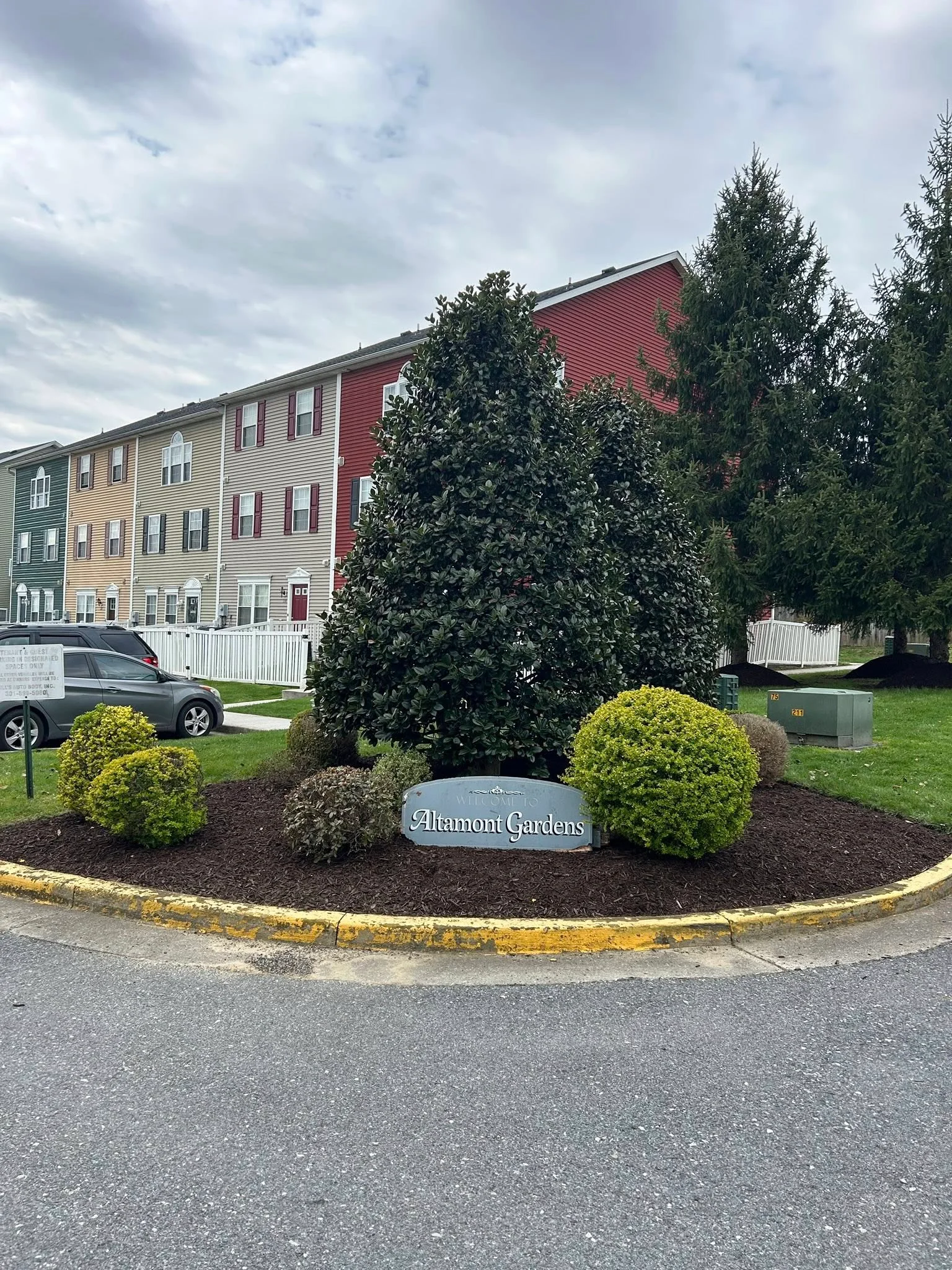 Mulch bed with evergreen shrubs and ornamental tree at residential entrance sign