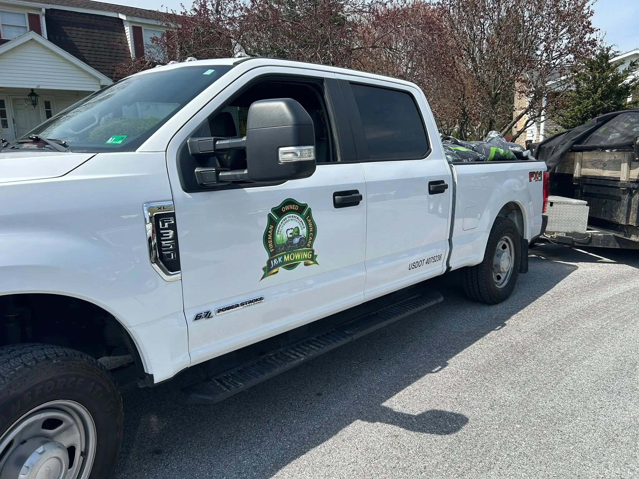 White pickup truck with custom vinyl wrap featuring green and gold mowing company logo and branding