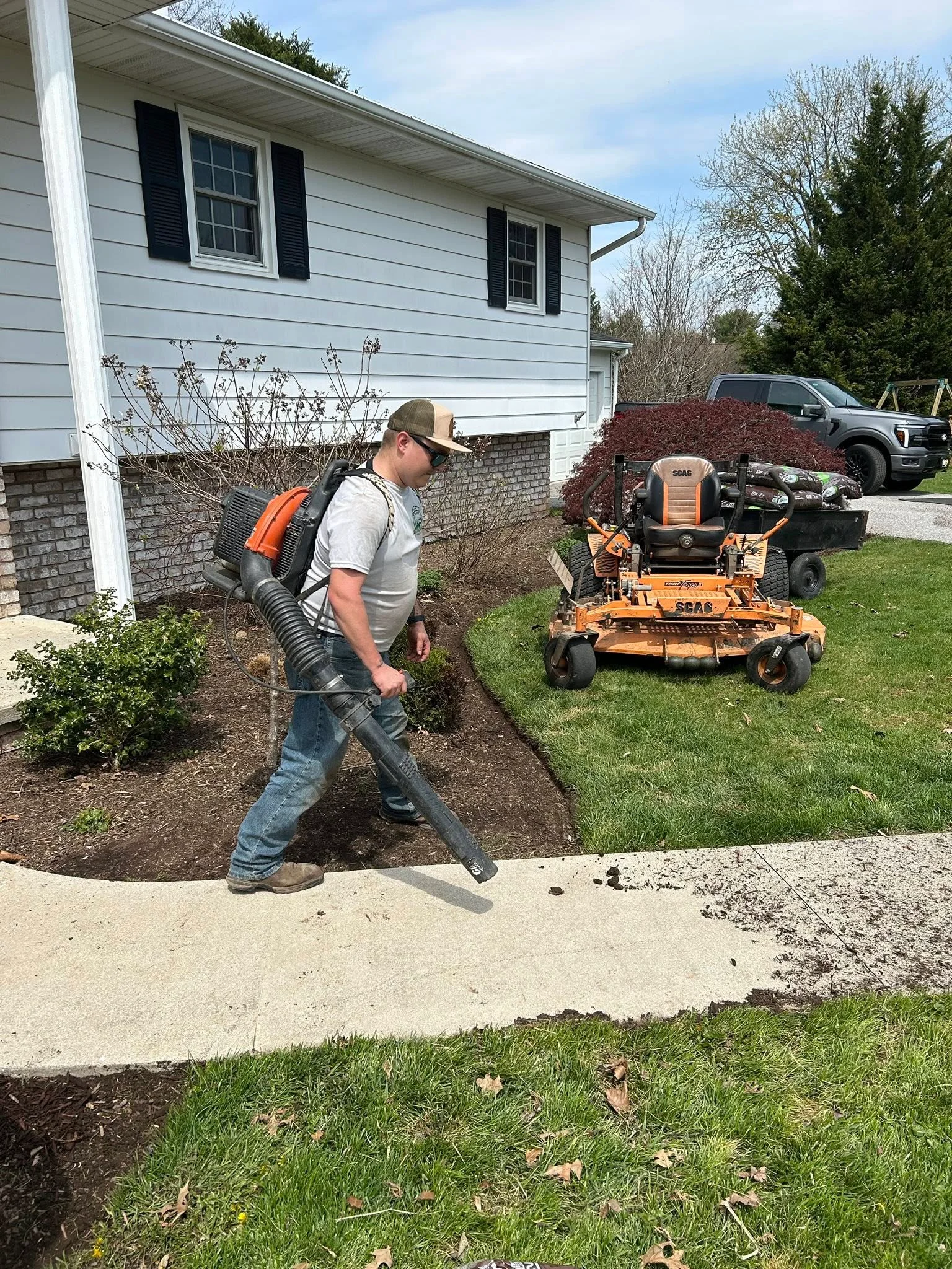 Lawn care technician using backpack blower to clear debris from landscape bed near residential home