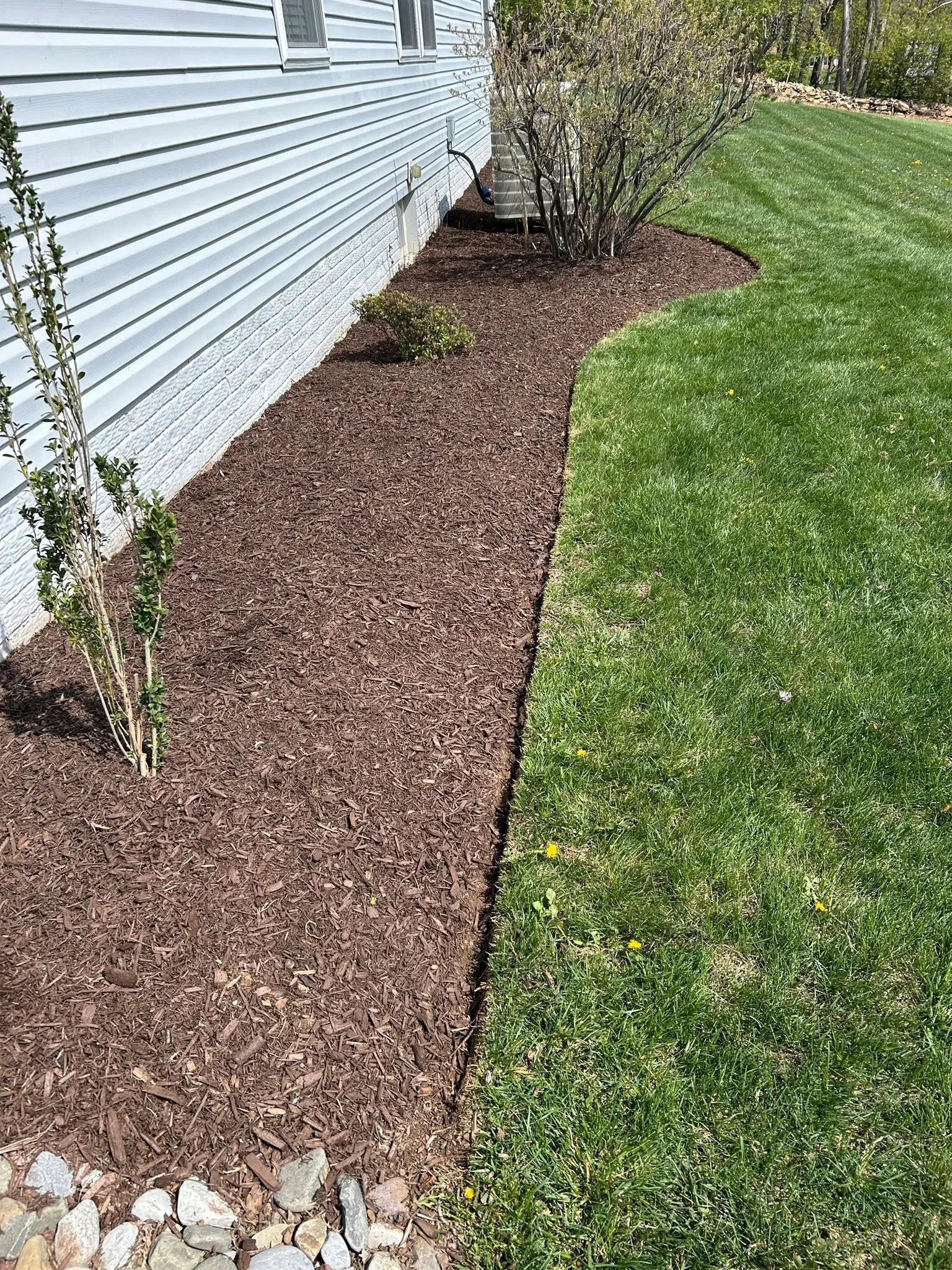 Brown mulch foundation bed with shrubs along white vinyl siding and stone edging