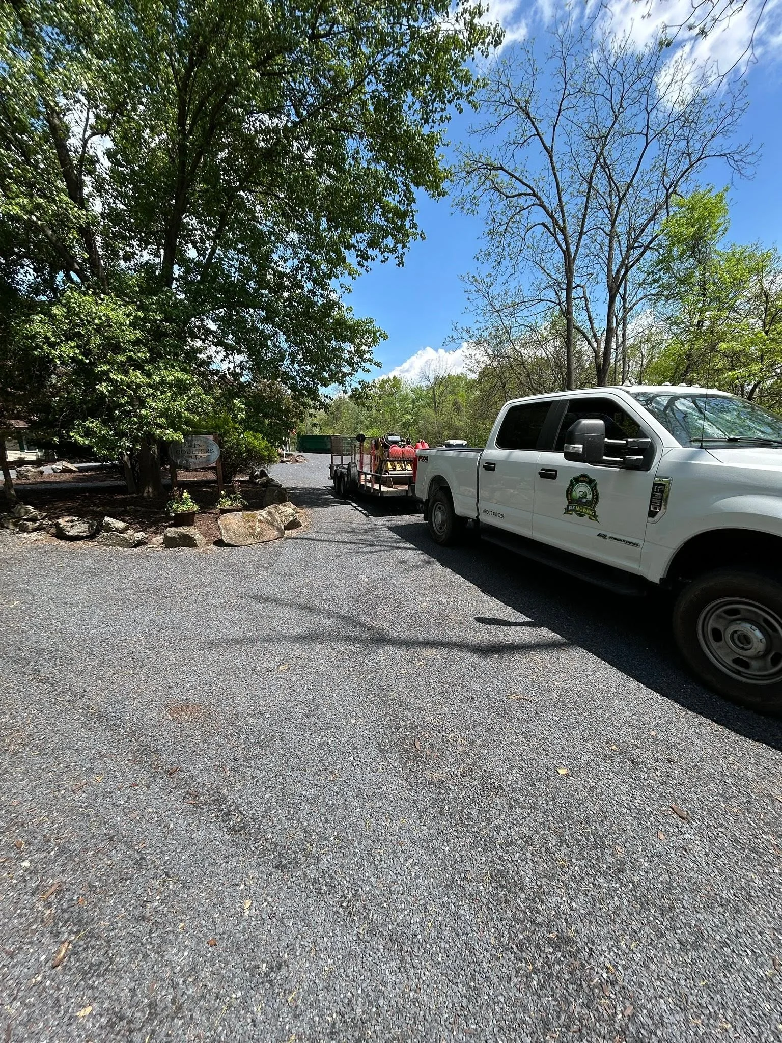 Gravel driveway with mature trees, stone edging, and service truck at commercial property