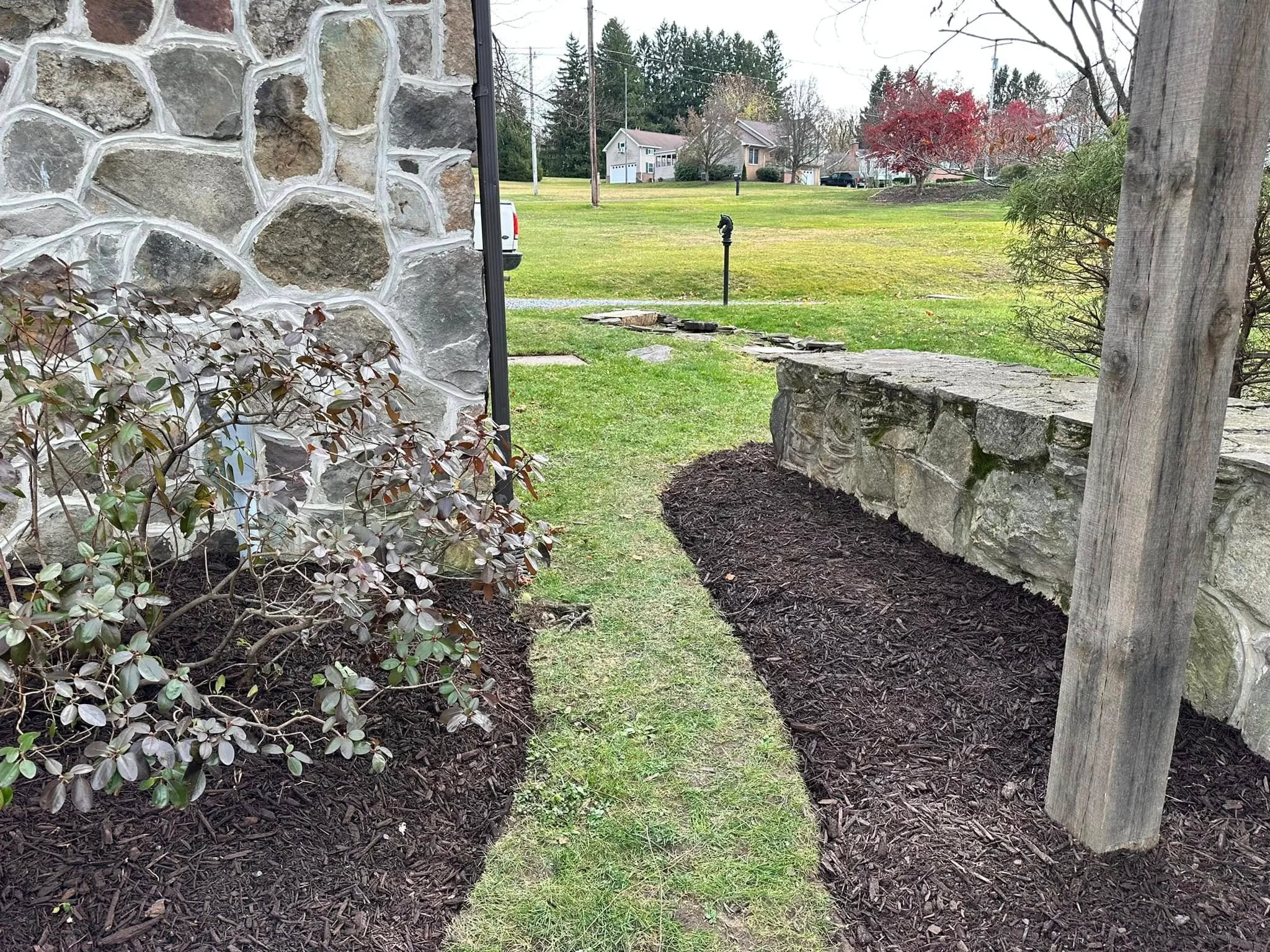 Dark mulch in landscape beds with stone wall, wooden posts, and established plantings